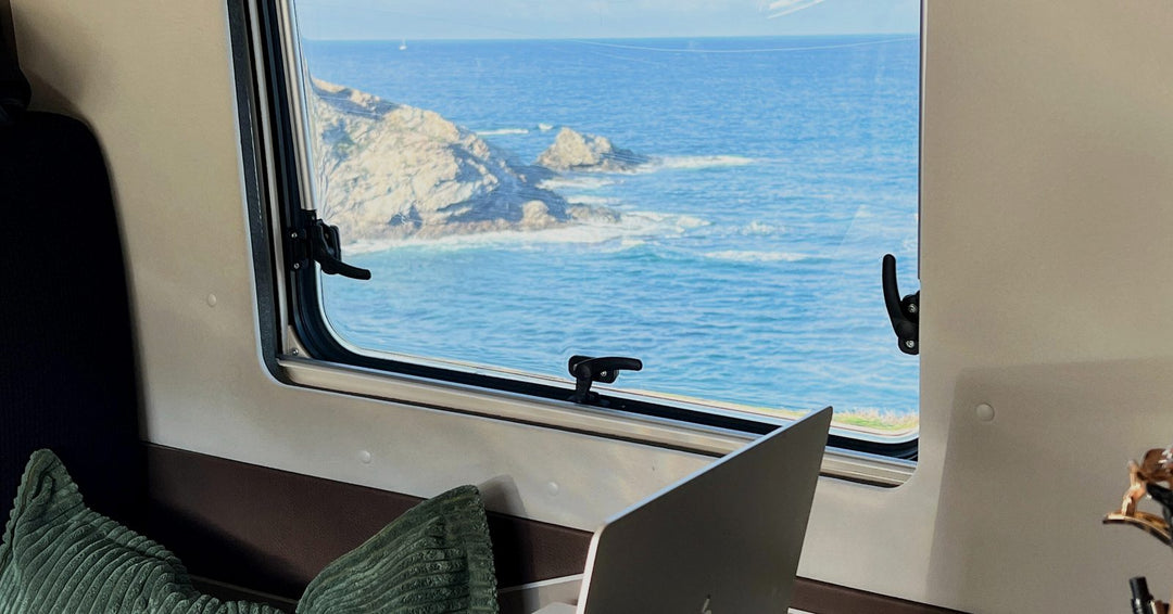 Arbeitsplatz im Campervan mit Laptop am Fenster, draußen Meer und Felsküste auf Sardinien