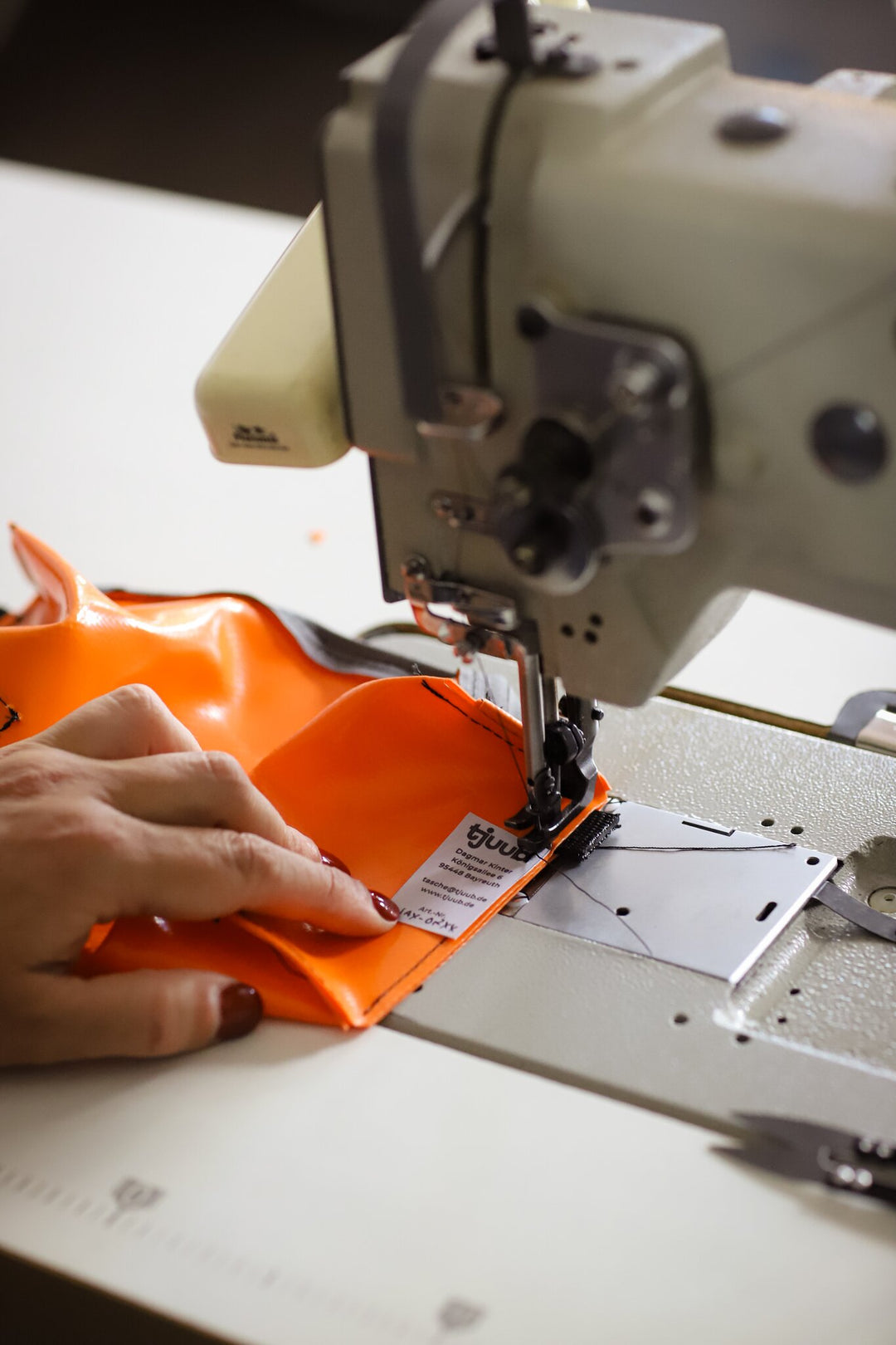 Hände vernähen eine orange Tasche aus recycelter LKW-Plane an der Nähmaschine.