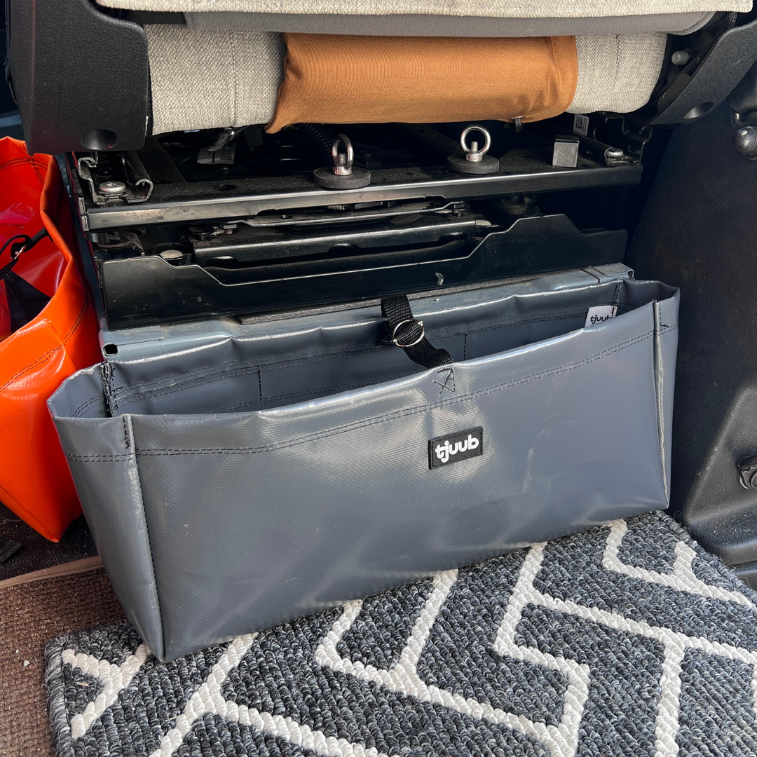 Grauer Organizer Muddus hängt magnetisch an der Sitzkonsole im Campervan, daneben eine orange Packtasche.
