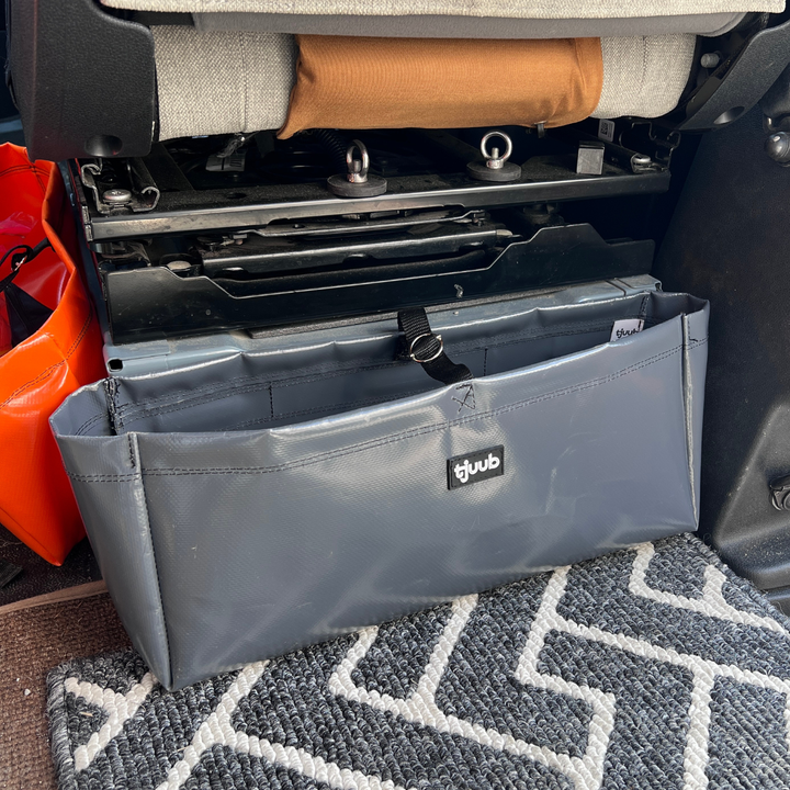 Grauer Organizer Muddus hängt magnetisch an der Sitzkonsole im Campervan, daneben eine orange Packtasche.