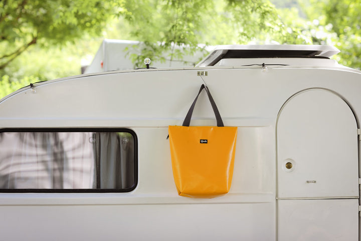 Gelbe tjuub Tasche Lassen hängt an einem weißen Wohnwagen, Vanlife Situation.