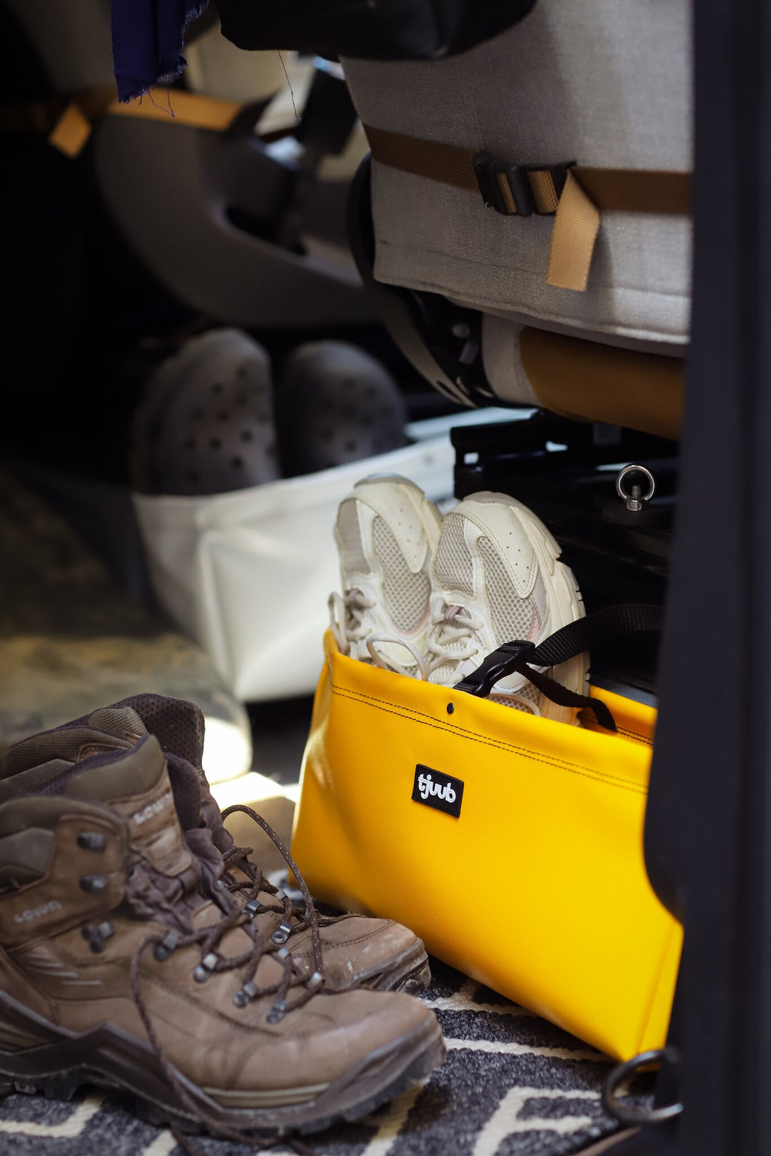 Gelbe tjuub Tasche Muddus als Untersitz-Stauraum im Camper, daneben Wanderschuhe.