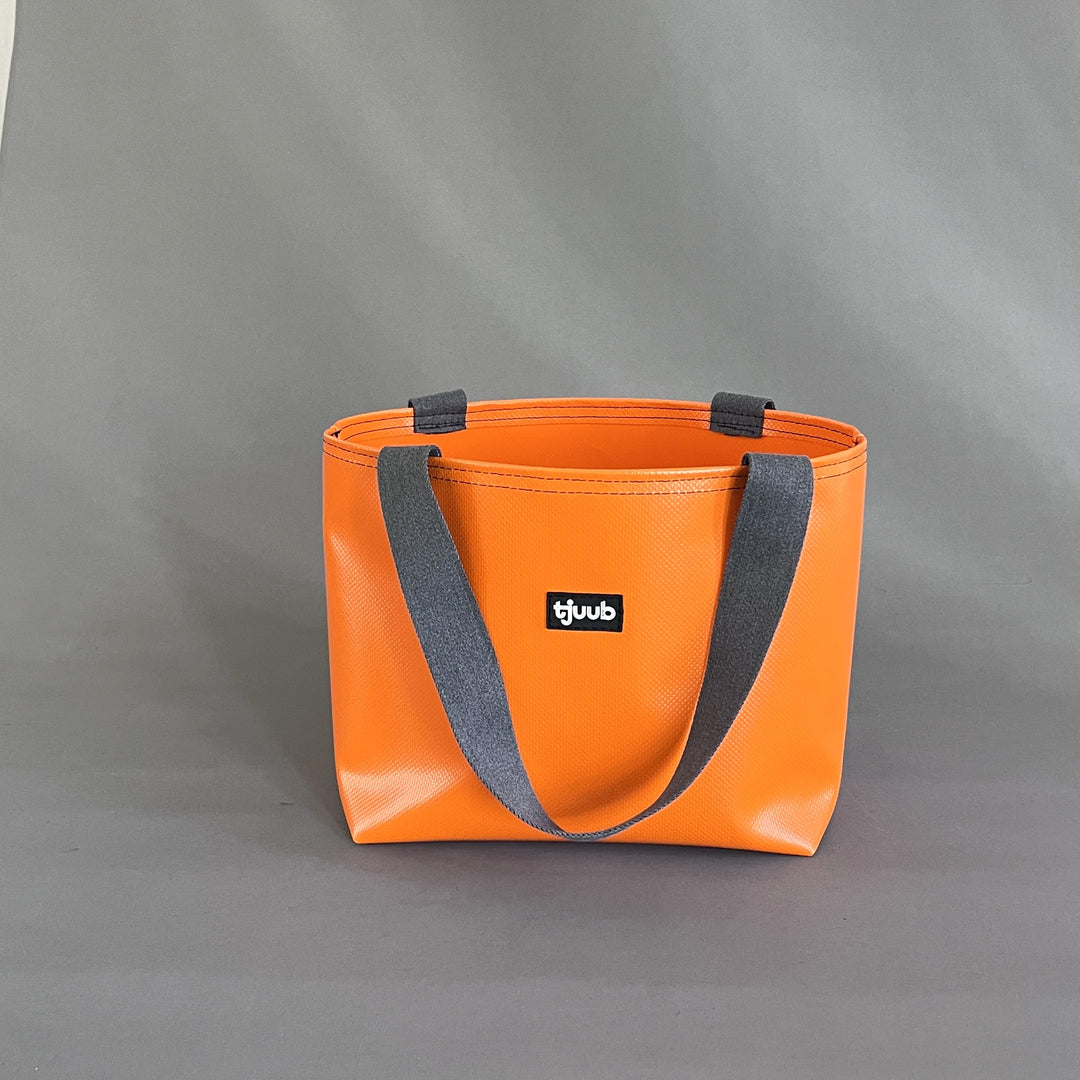Orange Tasche Sila ohne Reißverschluss aus LKW-Plane mit grauen Gurtbandträgern, Studioaufnahme.