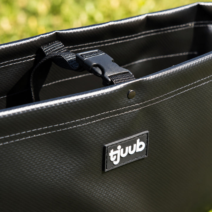 Nahaufnahme Muddus Organizer in Schwarz: doppelt genähte Oberkante, Steckschnalle am Gurtband und tjuub-Label.