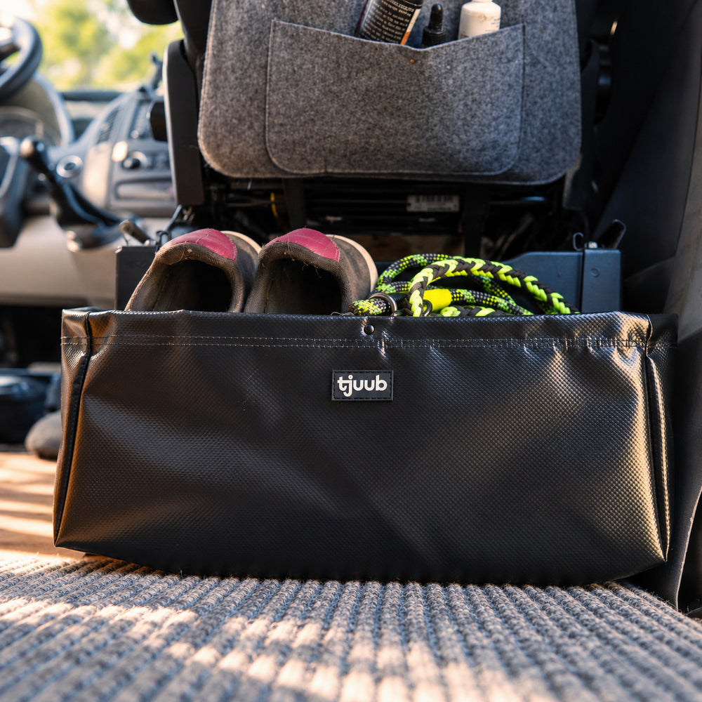 Magnetischer Organizer Muddus in Schwarz aus LKW-Plane an der Sitzkonsole im Campervan, darin ein Paar Schuhe und die Hundeleine.