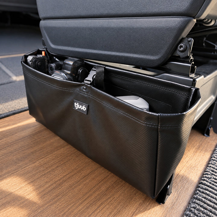 Muddus Organizer in Schwarz hängt unter dem Drehsitz im Wohnmobil an der Konsole, der Sitz bleibt drehbar, darin Kamera und Kleinkram.