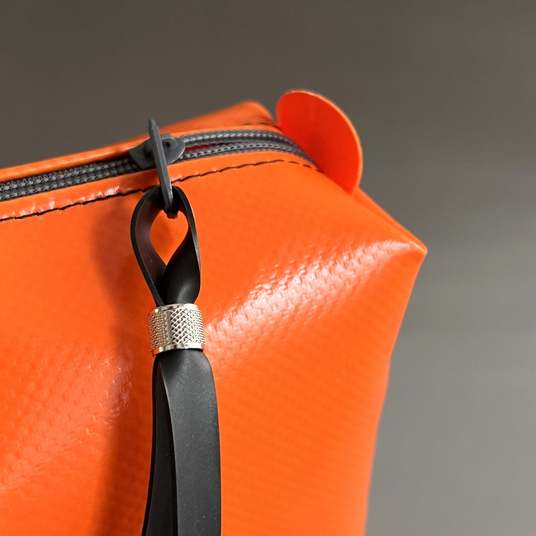 Detailaufnahme der orangen Umhängetasche Una von tjuub mit grauem Reißverschluss und schwarzem Zugband.